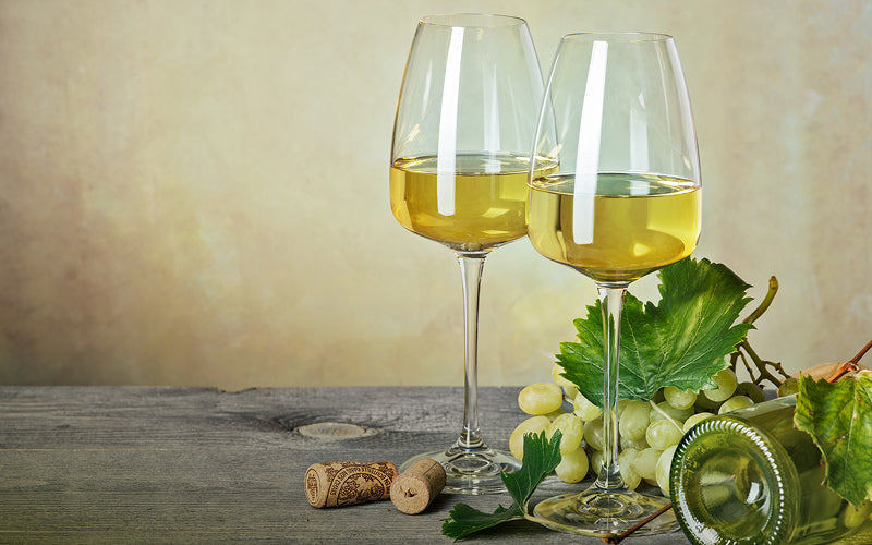 Two glasses of white wine with grapes and corks.