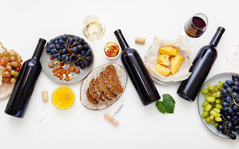 Flat lay of wine bottles, cheese, bread, and grapes.